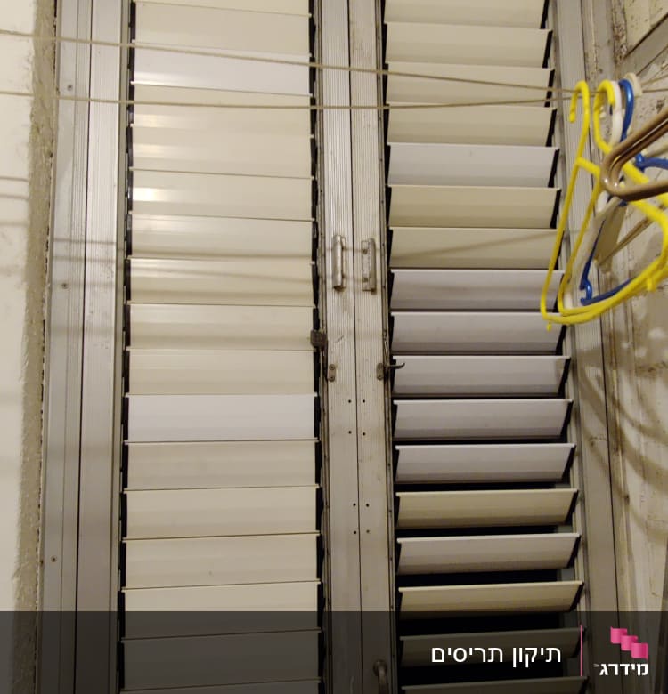 תריסים לבנים עם מסגרת מתכת בחלון